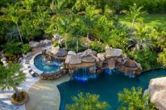 Aerial perspective of a waterslide winding into a lagoon-style pool with tropical trees.