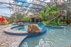 Waterslide framed by vibrant tropical plants and stonework in a custom outdoor pool setting