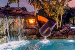 Poolside view of a slide exit area with rock grotto and surrounding tropical foliage.