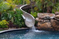 Close-up of a backyard waterslide with  natural stone and lush greenery .