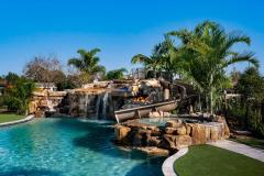 Resort-style backyard pool featuring a curved waterslide integrated into rock formations.