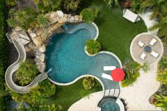 Aerial perspective of a waterslide winding into a lagoon-style pool with tropical trees.