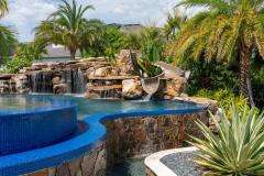 Twisting waterslide dropping into sparkling blue water with outdoor greenery backdrop.